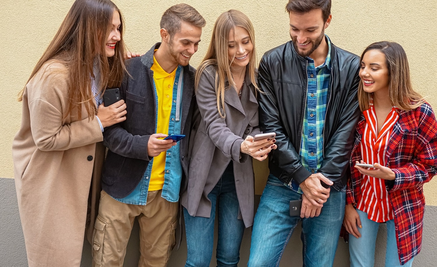 A group of young people standing next to each other looking at each others smartphone.